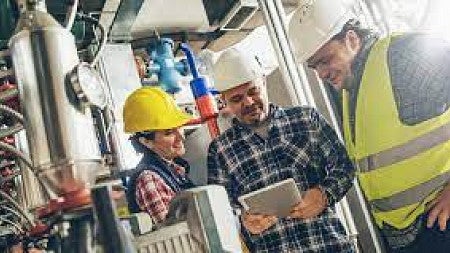 Three professionals wear hardhats as they talk animatedly.