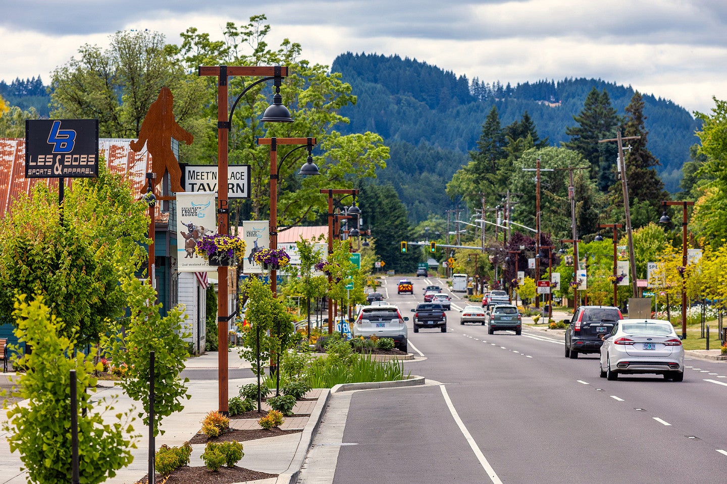 Philomath city street with greenery, store signs, and mountains in the background