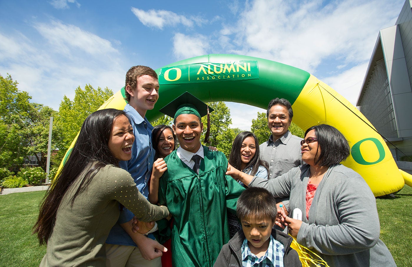 A family posing with their graduating Duck in front of the alumni arch in the grass outside the Ford Alumni Center.