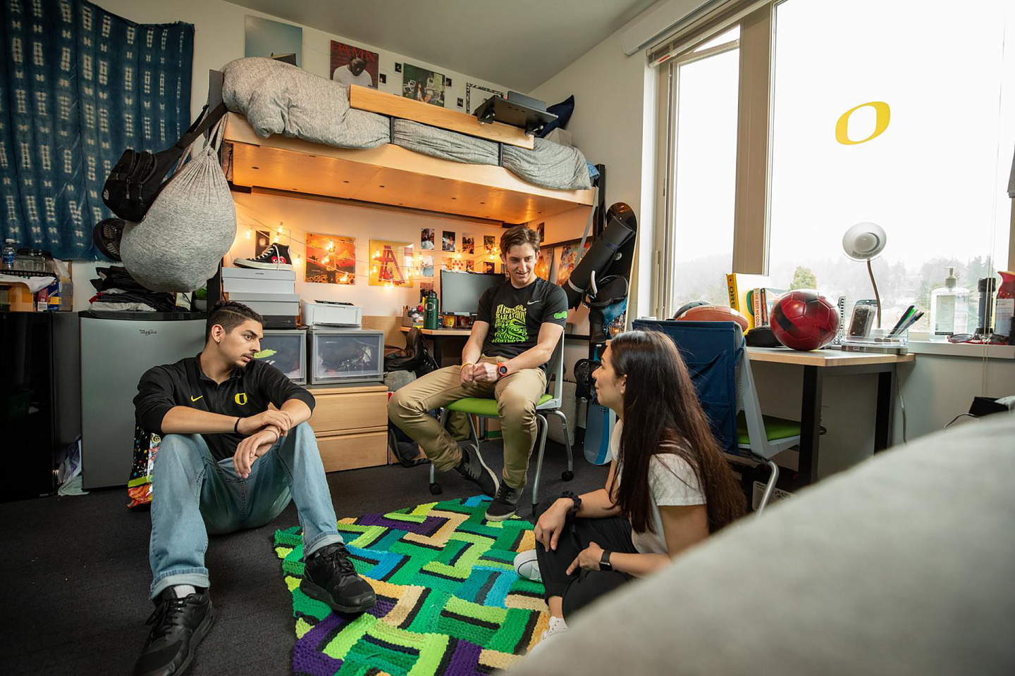 three students sitting down in a large dorm room