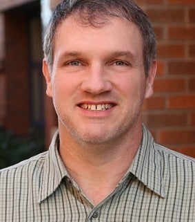 Professor in plaid shirt in front of brick wall