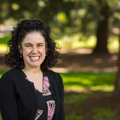 Smiling woman with dark brown curly hair wearing black sweater and black and pink blouse
