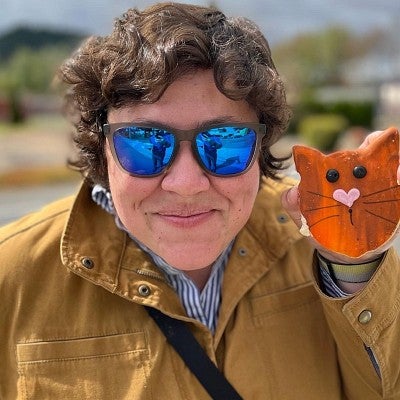 Woman in sunglasses smiling holding a cat-face shaped cookie