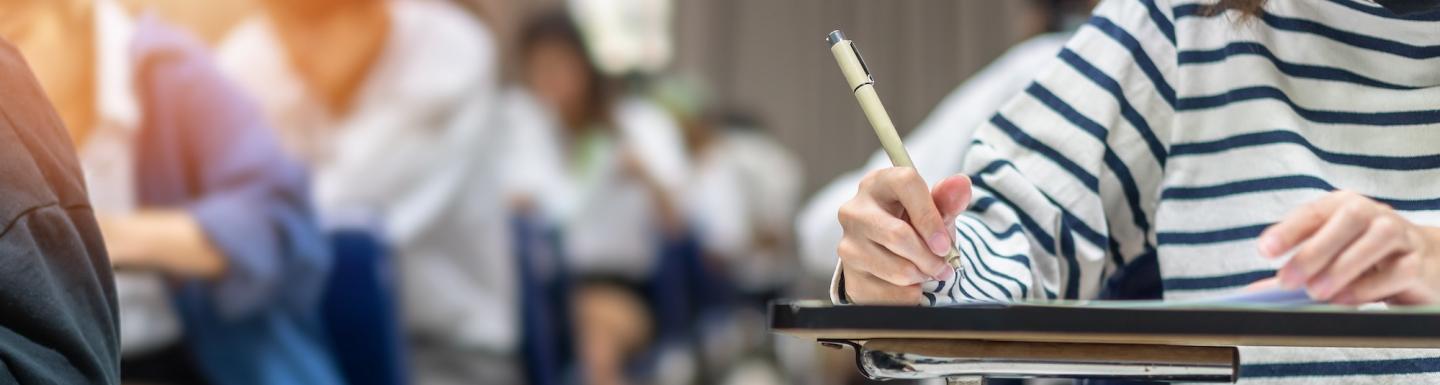 A young woman sitting at a school desk and writing