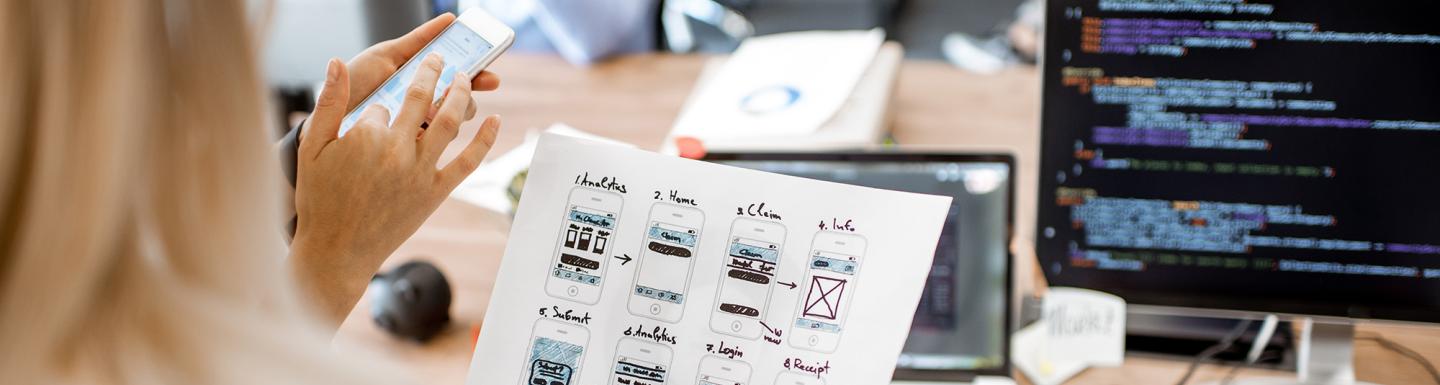 Developers or web designers developing mobile application in the office, close-up on phone and paper sketches