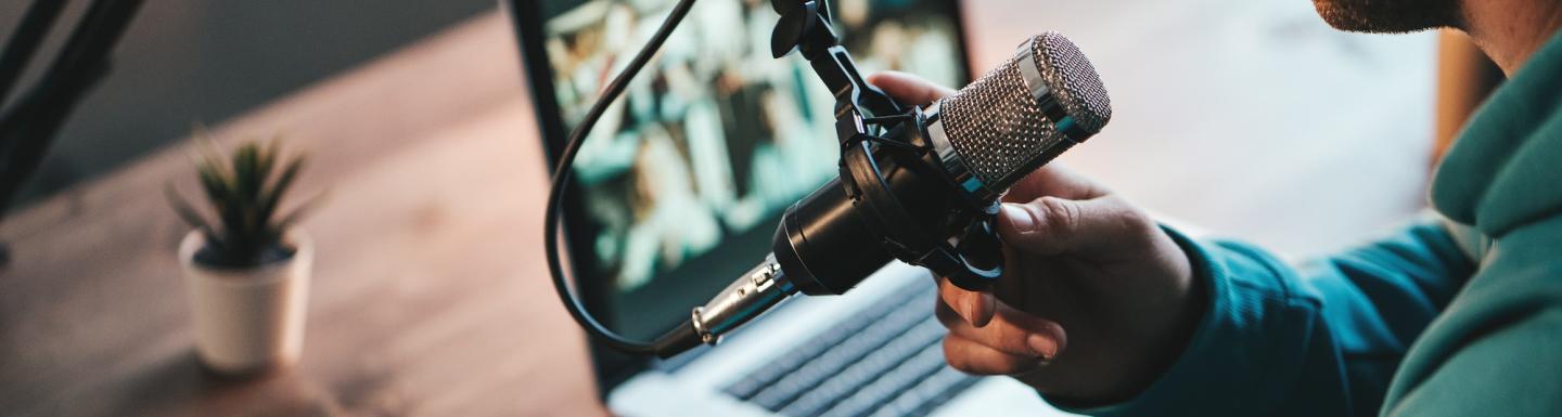 A man host streaming his audio podcast using microphone and laptop at his small broadcast studio, close-up