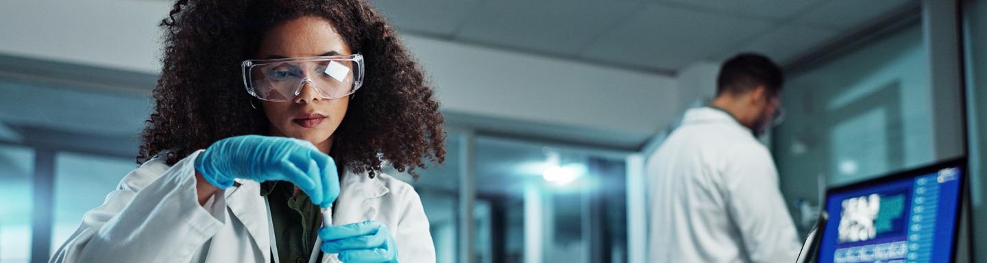 A black woman in a white lab coat holds a vial for testing in laboratory