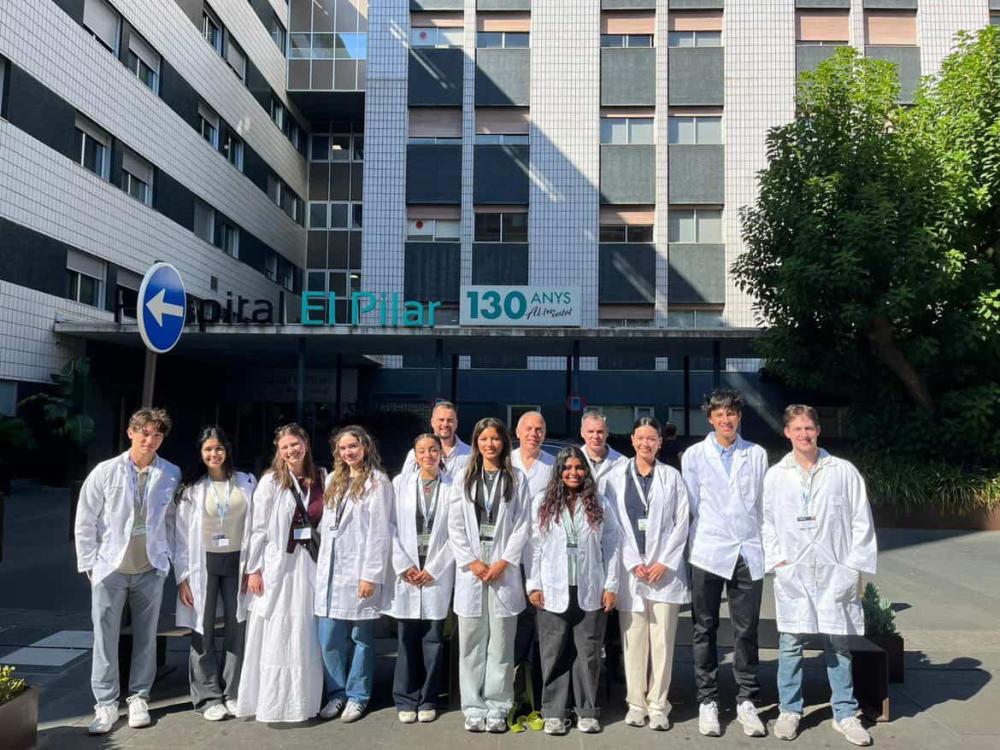 Cohort of pre-med students outside a Spanish hospital wearing lab coats and name tags