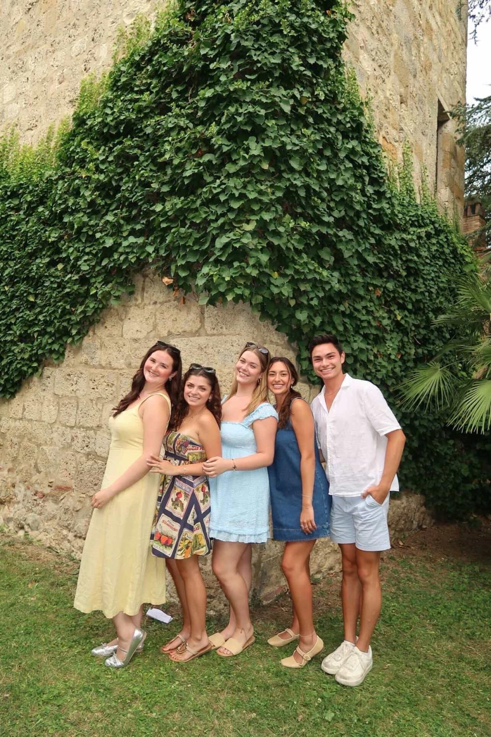 Five students smiling for a photo by a cobblestone building covered in vines