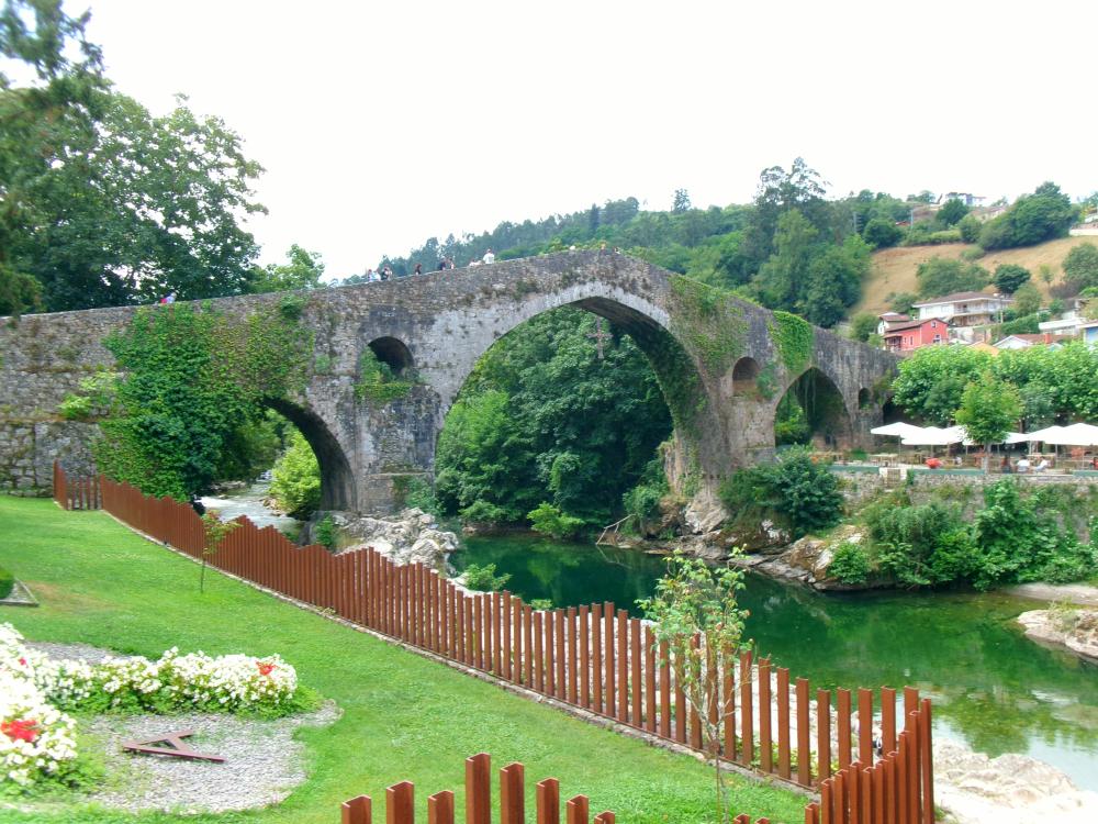A picturesque photo of the spanish countryside with a bridge and stream 