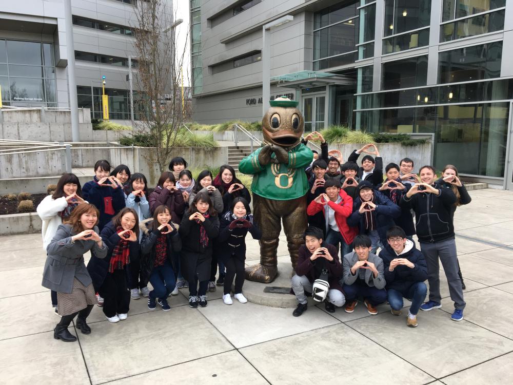Group of students "throwing their o" in front of a Duck statute