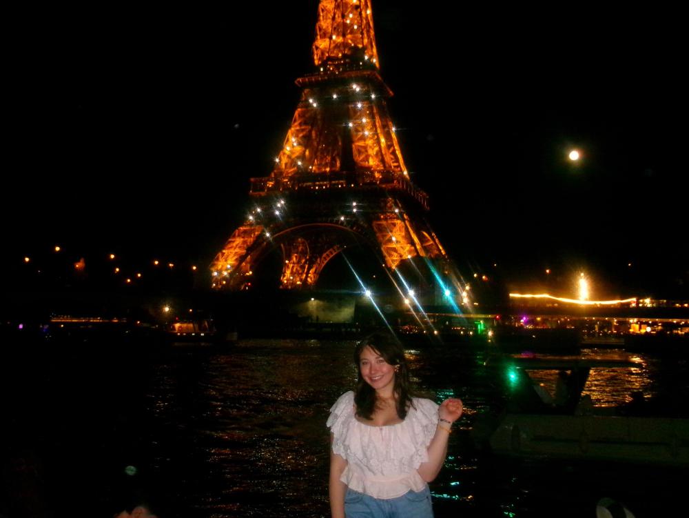 Giana smiling by the River Seine at night with the Eiffel Tower sparking in the background