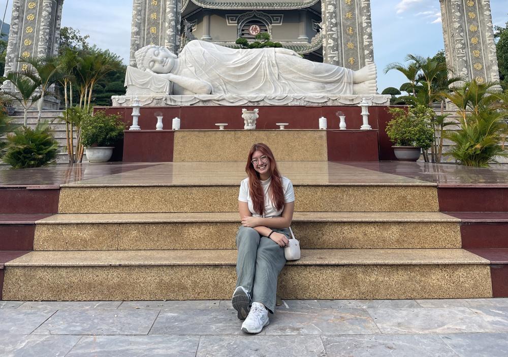 Young woman sitting on some steps in front of a Vietnamese temple