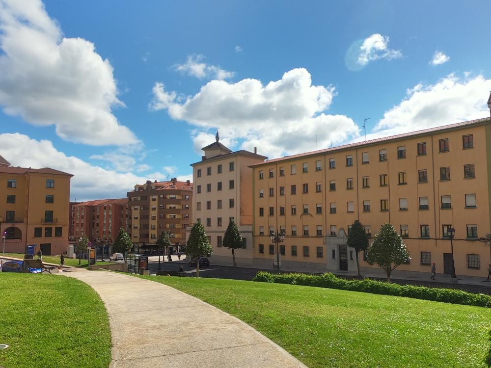 A concrete path amongst grass with a large building in the background against a blue sky with white clouds