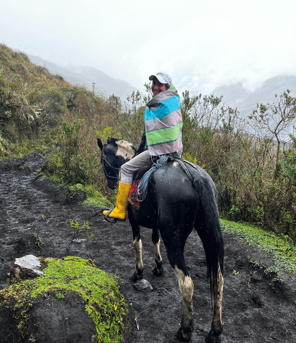 Women riding a horse along a muddy trail on a rainy day.