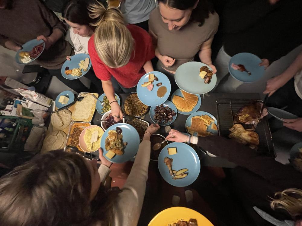 A group of students gathers around with half full plates of food, scooping various dishes onto their plates