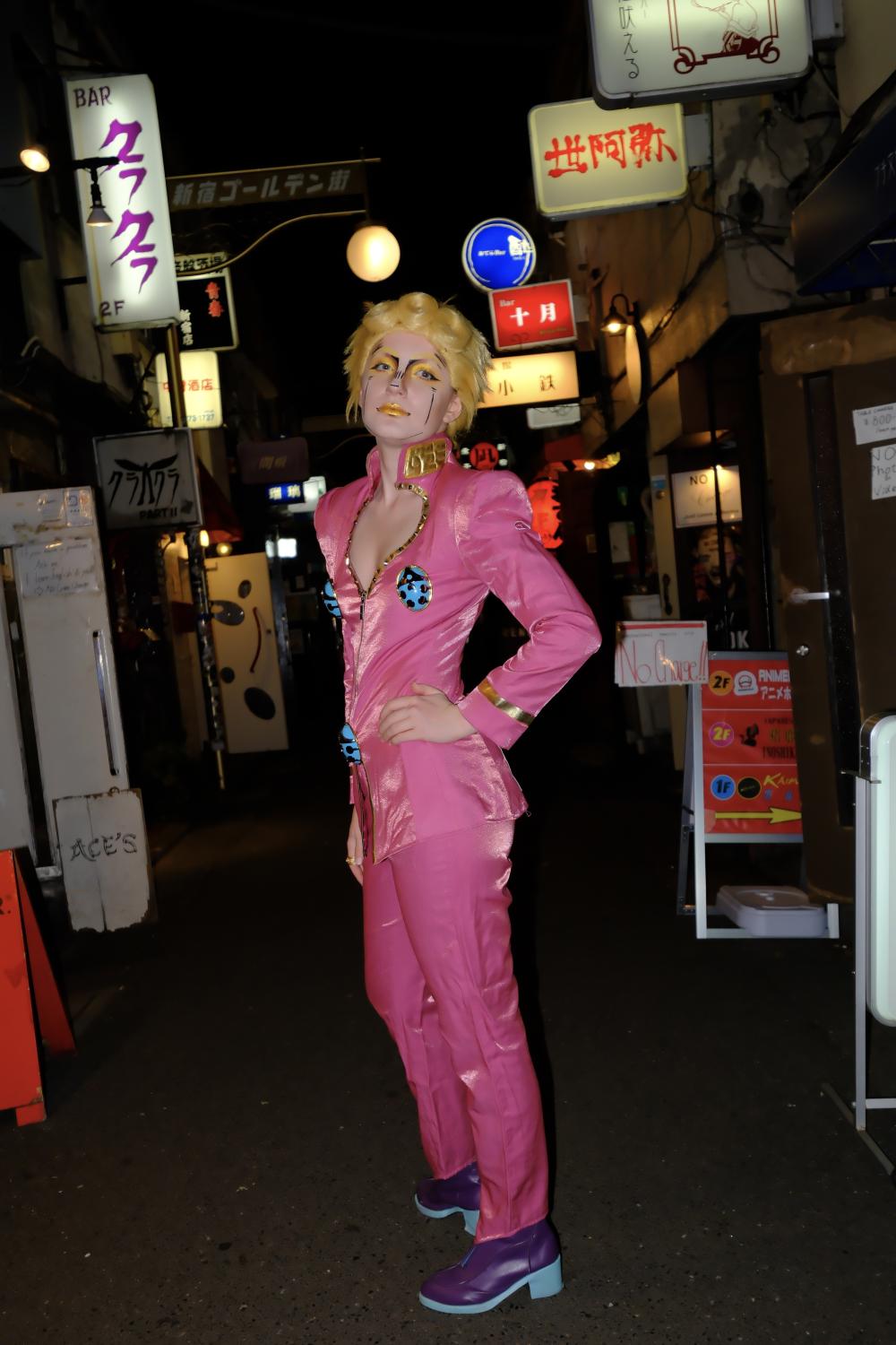 Elizabeth in a pink jumpsuit in cosplay, looking at the camera; the rest of the backgroun is dark with some lit-up signs