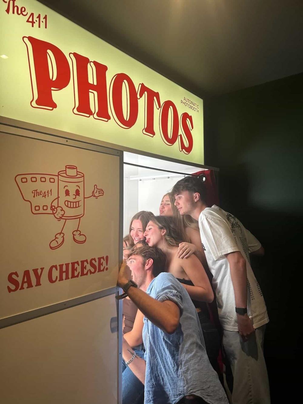 Group of students crowding into a photobooth that says "Say Cheese" outside