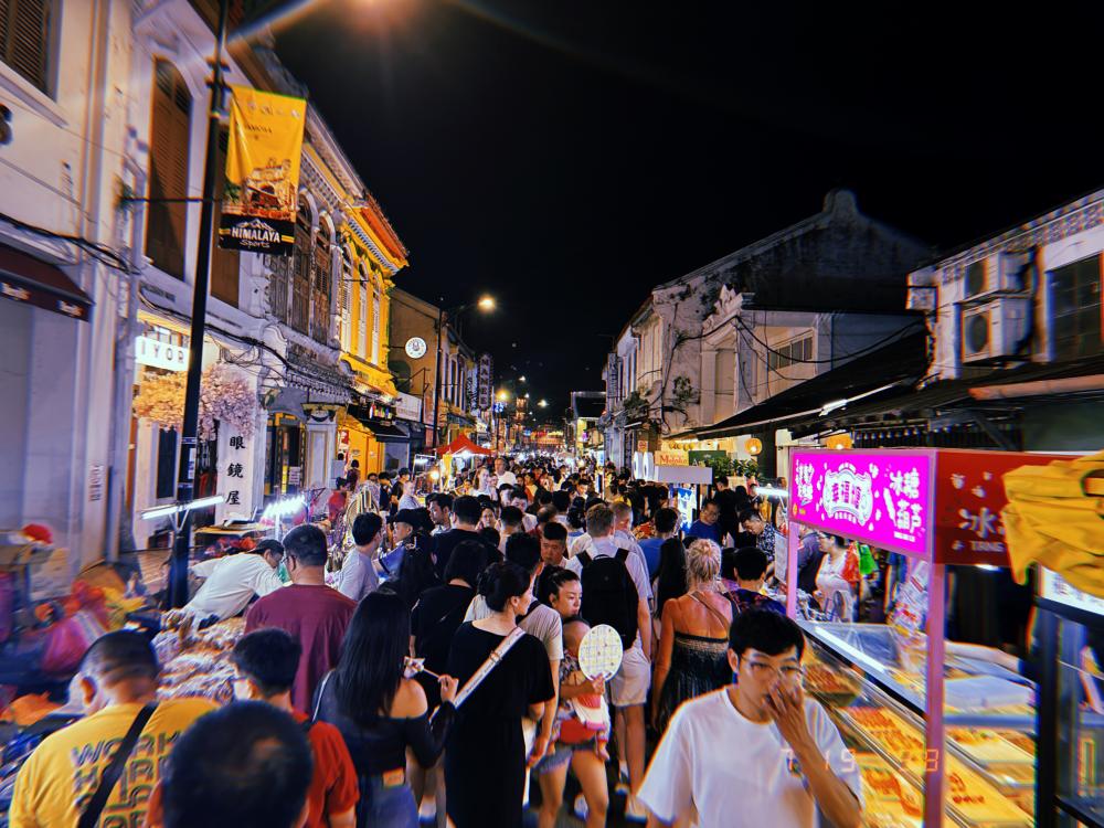 Crowds of people in a narrow street at night, lit by food stalls on both sides