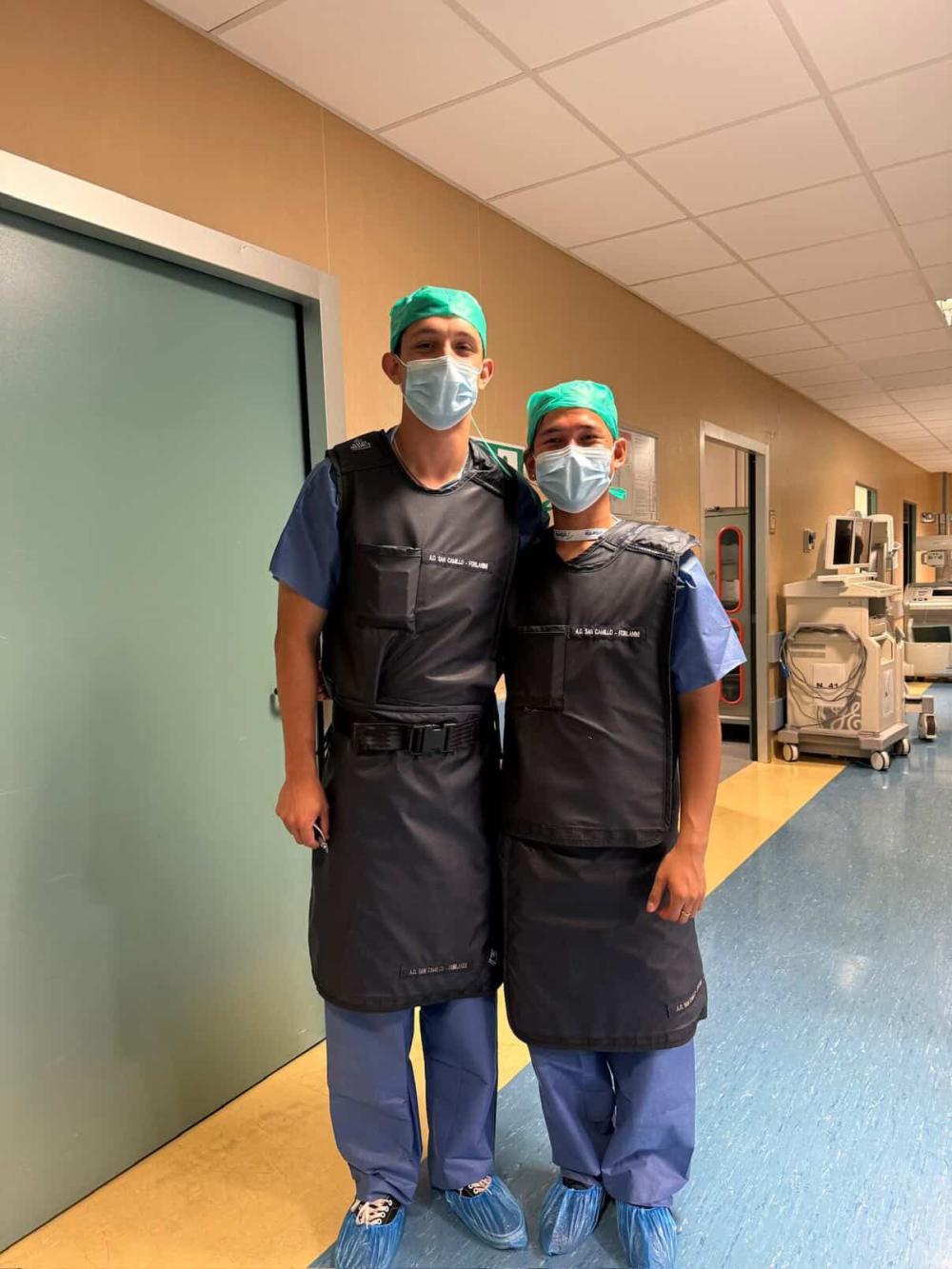 Densel smiling with another pre-med student in scrubs in a hospital