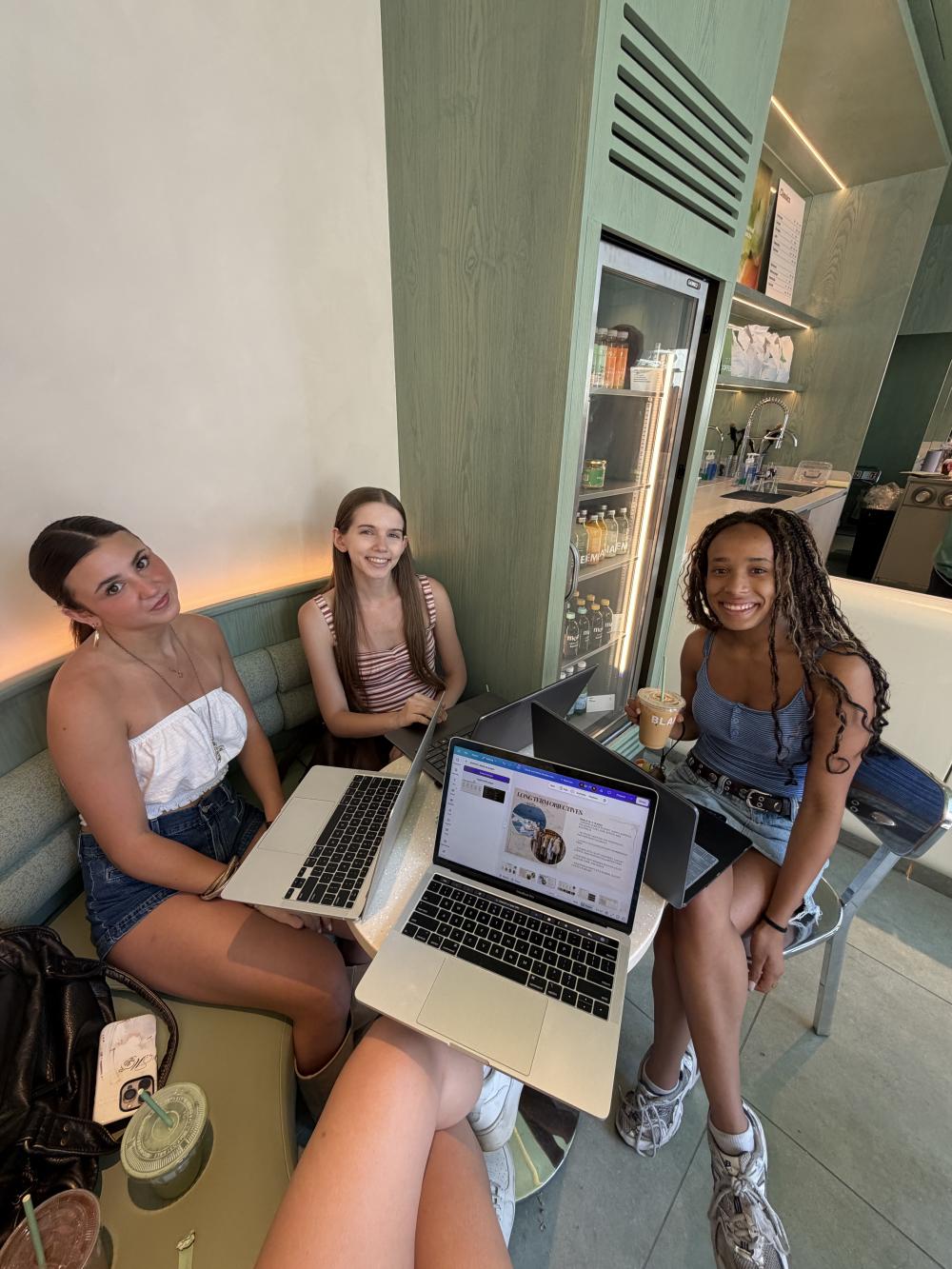 3 people sit around a small circle table with their laptops, smiling at the camera