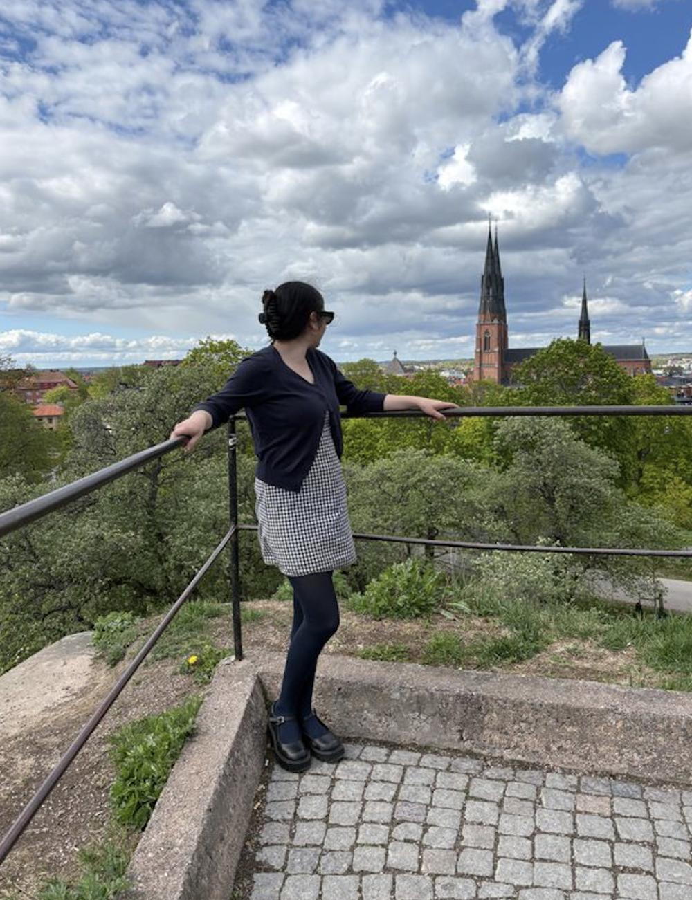 Ava looking out in the distance to a brick cathedral in Stockholm under a partly cloudy sky