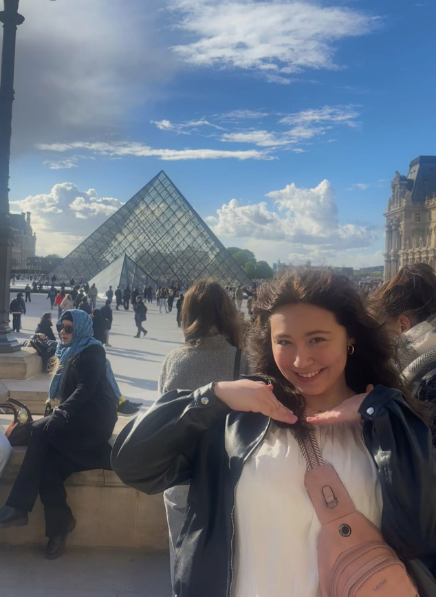 Giana smiling with her hands cupping her face in front of the Louvre Museum in Parise