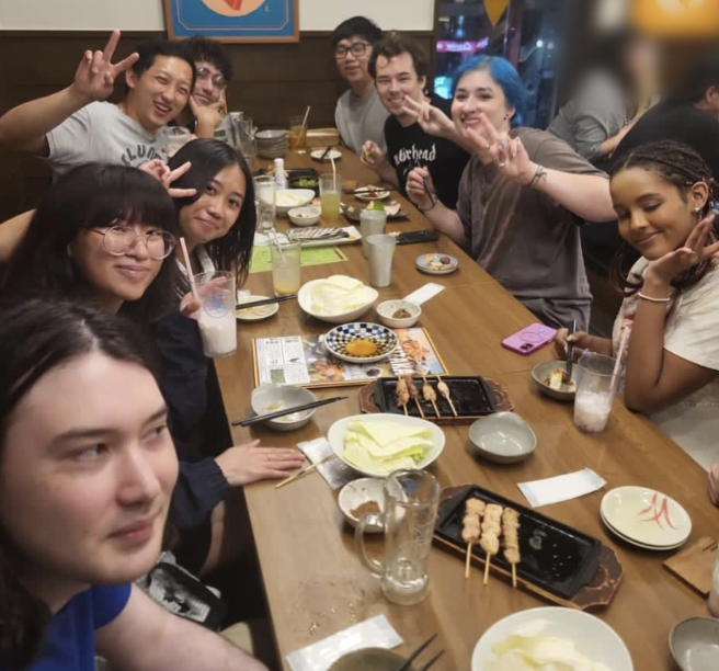9 people are seated at a long dinner table in a restaurant, posing for the camera