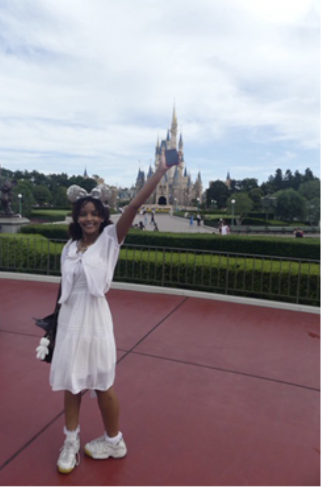 Sara stands in a white dress with a silver Mickey Mouse ear headband in front of a castle at Tokyo Disneyland