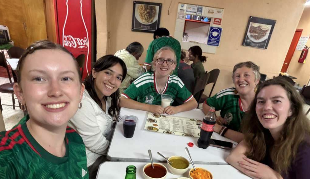 5 people smile at the camera around a table with food and Mexico soccer jerseys on