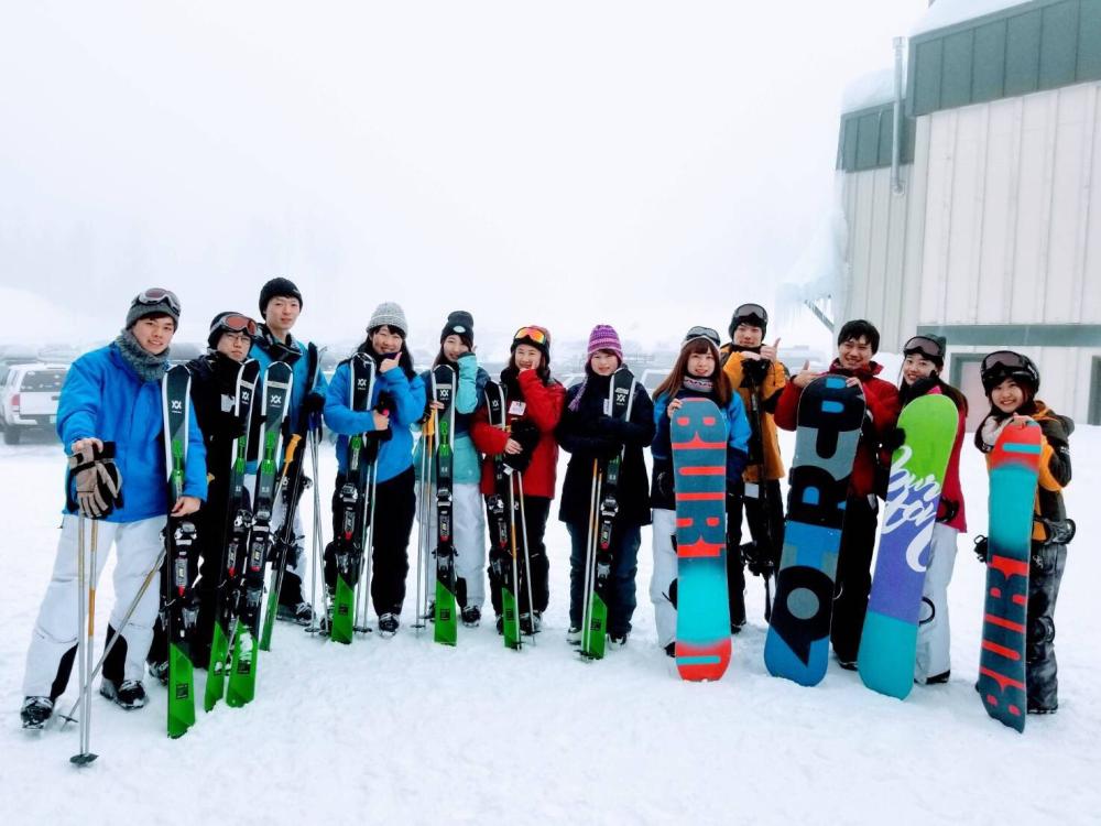 Group of people standing in snow holding a snowboard in their hands 