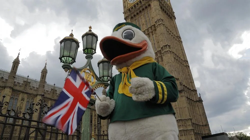 The Duck mascot holding a UK flag in front of the Big Ben tower