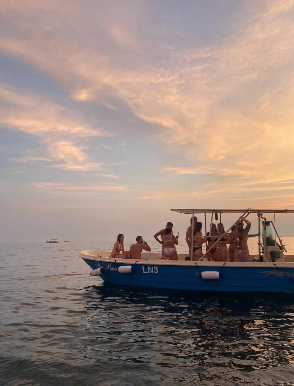 Ten people enjoying the sunset on a small boat at sea.