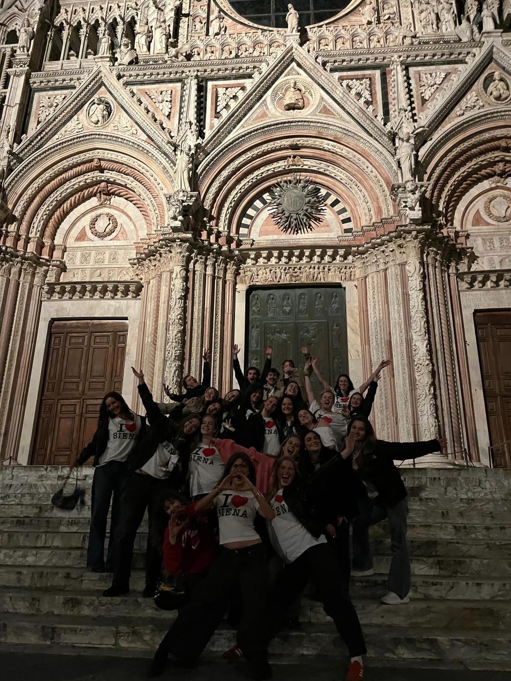 Cohort of students posing with their arms up on the steps of a church in Siena