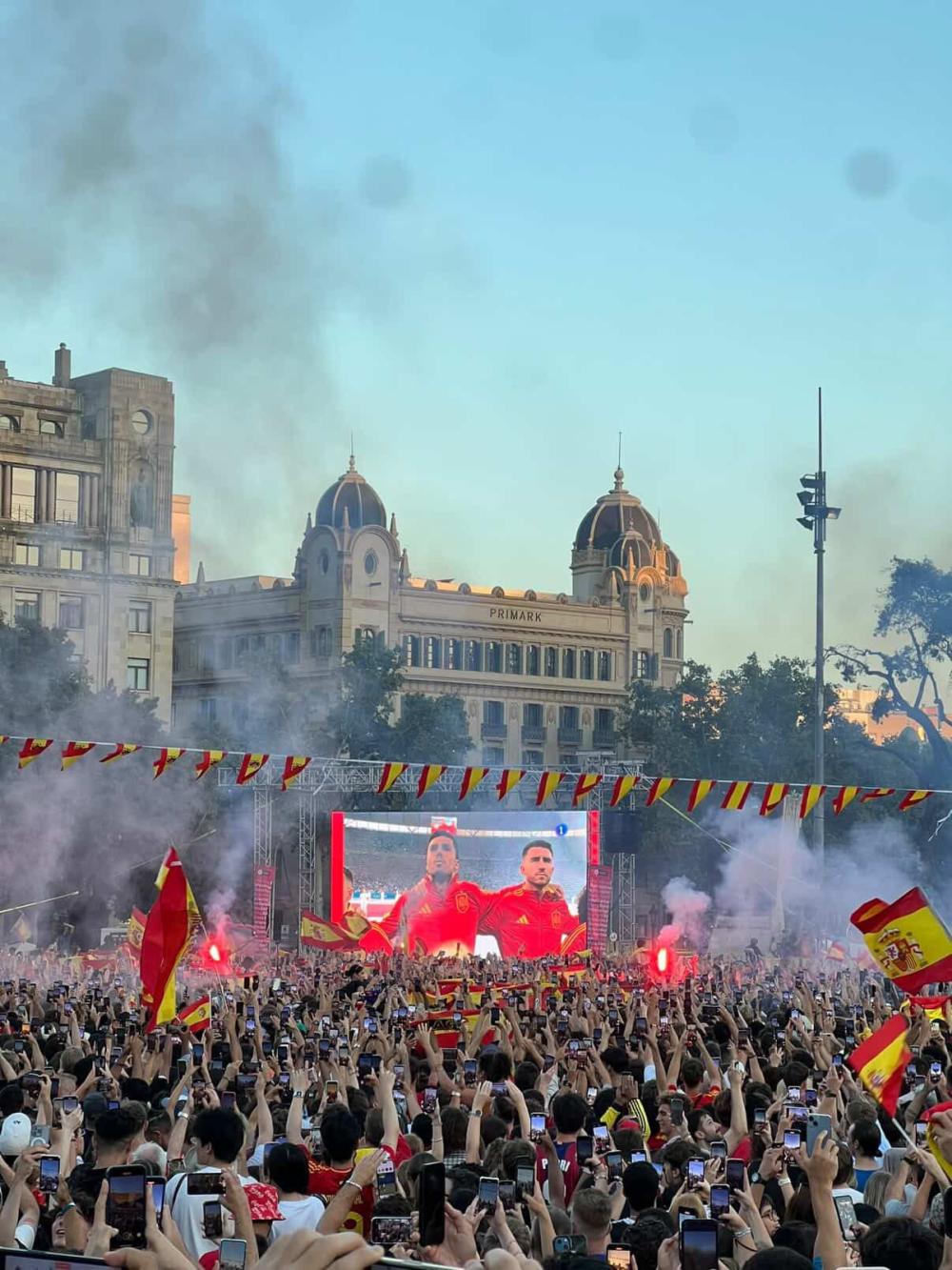 Outside celebration of locals cheering on a futbol game with Spanish flags and smoke in the air