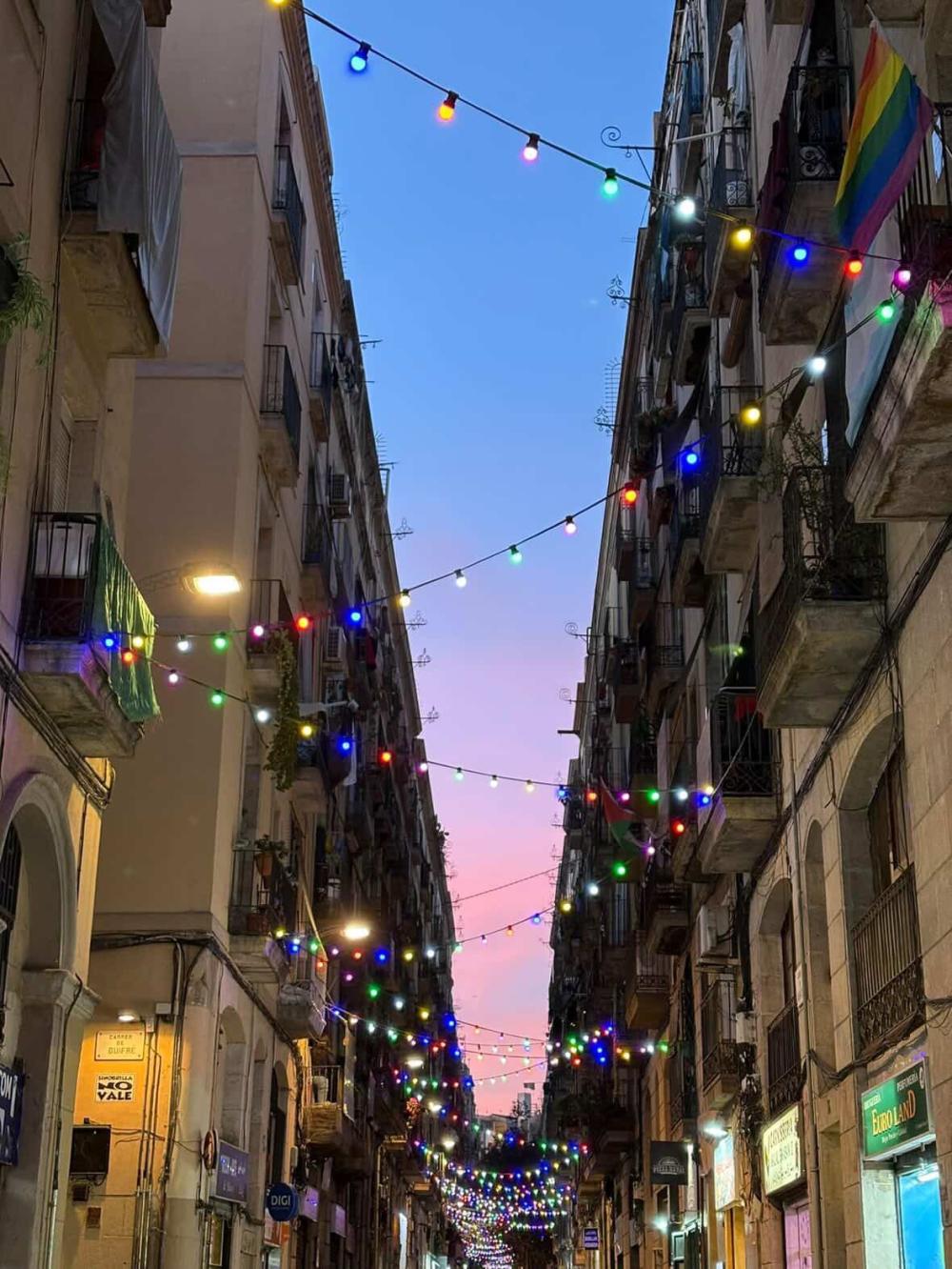 Spanish buildings during sunset with Christmas lights and a pride flag hanging above