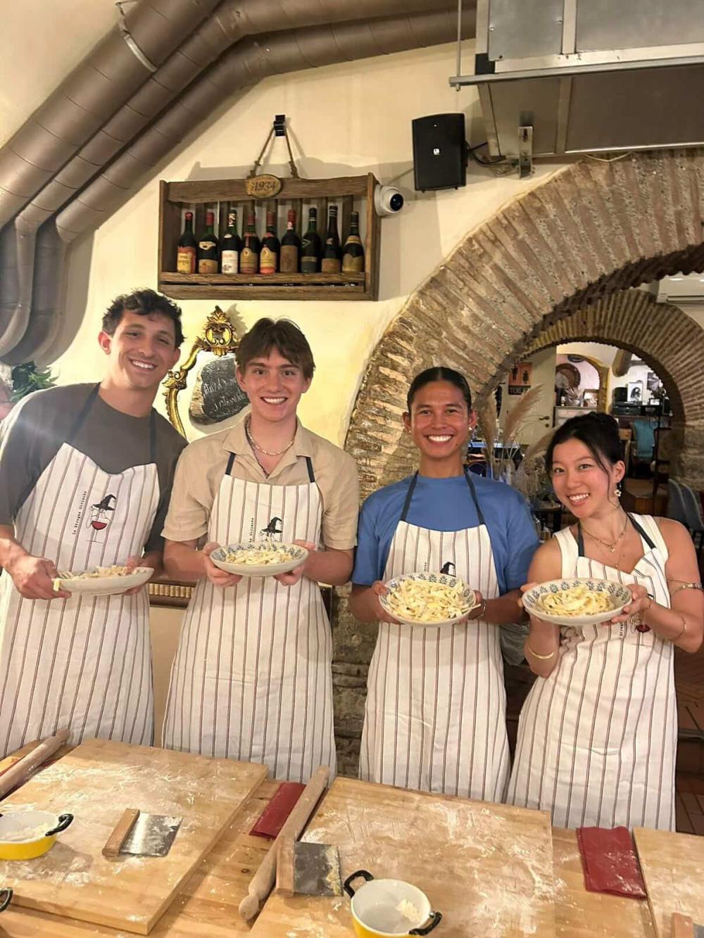 Four students smiling with aprons and fresh pasta during a cooking class