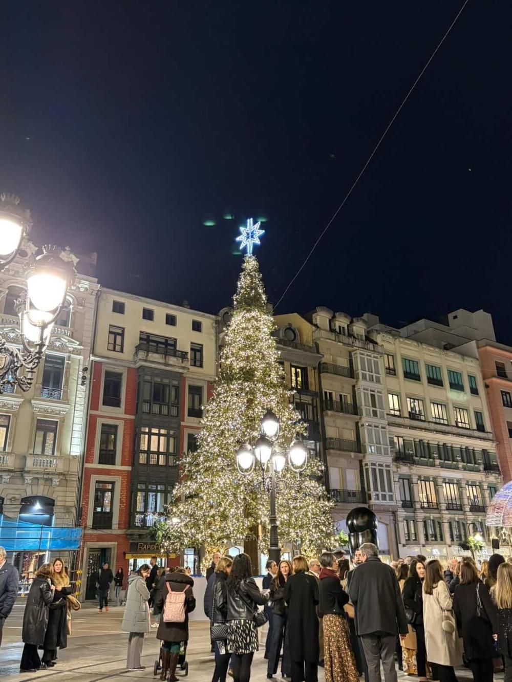 Spanish square with people gathering around a lit Christmas tree at night