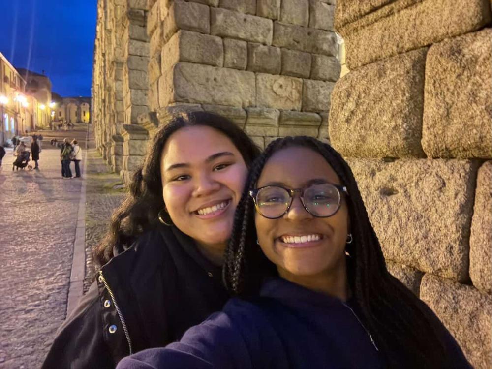 Ariel and a friend smiling by a cobblestone building during an evening in Spain