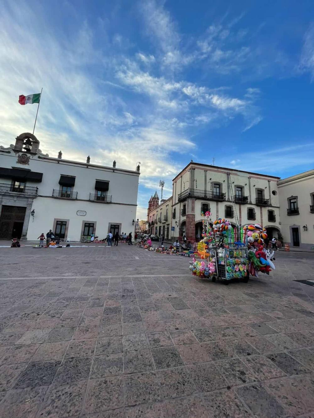 City square in Mexico with the Mexican flag waving above on a sunny day