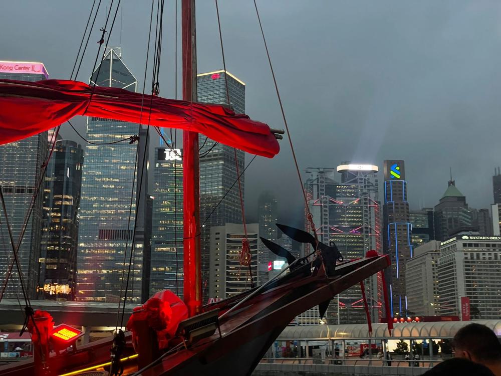 Skyline of Hong Kong under a cloudy grey night sky with a boat passing in front.