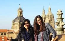 Two students pose in front of traditional buildings.