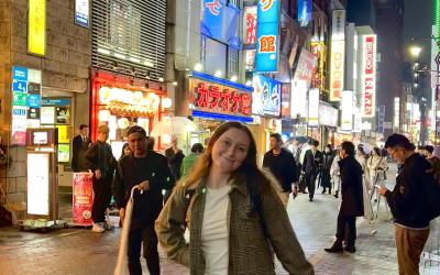 A young woman stands on a busy street in Tokyo at night 