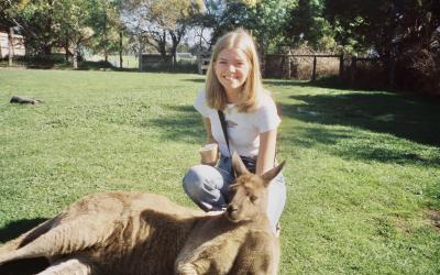 College-aged girl posing behind a kangaroo lying on its back in a park in Australia. 