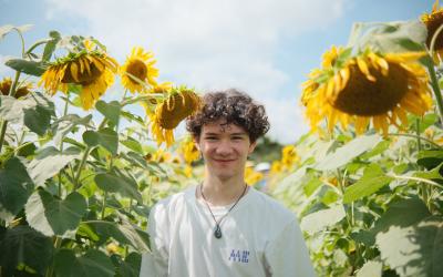 Person smiling in a field of vibrant sunflowers under a clear sky.