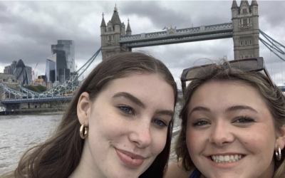 Two girls smiling for a selfie with the London bridge behind them. 