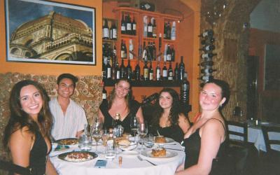 Film photo of five students gathered around a table in Italy enjoying dinner and wine