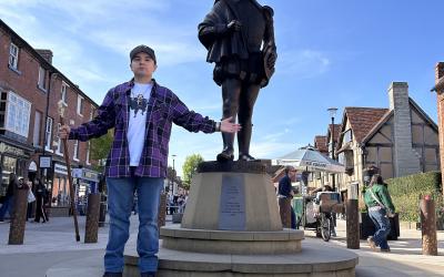 Isaiah standing in front of a William Shakespeare statue in London, holding a staff