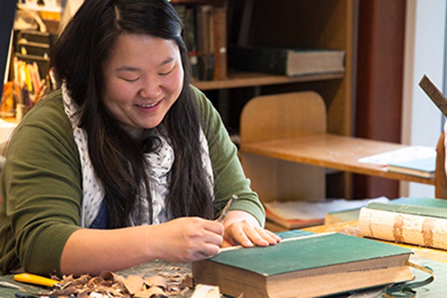 A woman with long, dark hair smiling and sitting at a table with books.