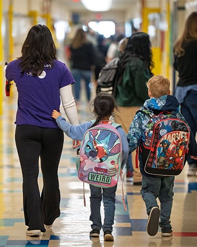 Back of Kaylin Kisor walking with two students in a school hallway